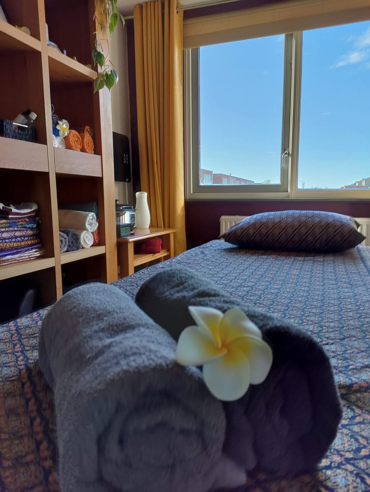 De massageruimte van Sabaai Thai Massage: massagetafel met Thaise stof, opgerolde handdoeken met een frangipanibloem en veel daglicht